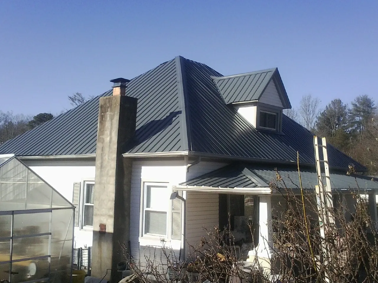 Dark blue standing seam metal roof on a white farmhouse with dormer — Slate & Tile Roof Repair by Roofing Brothers in Bent Mountain
