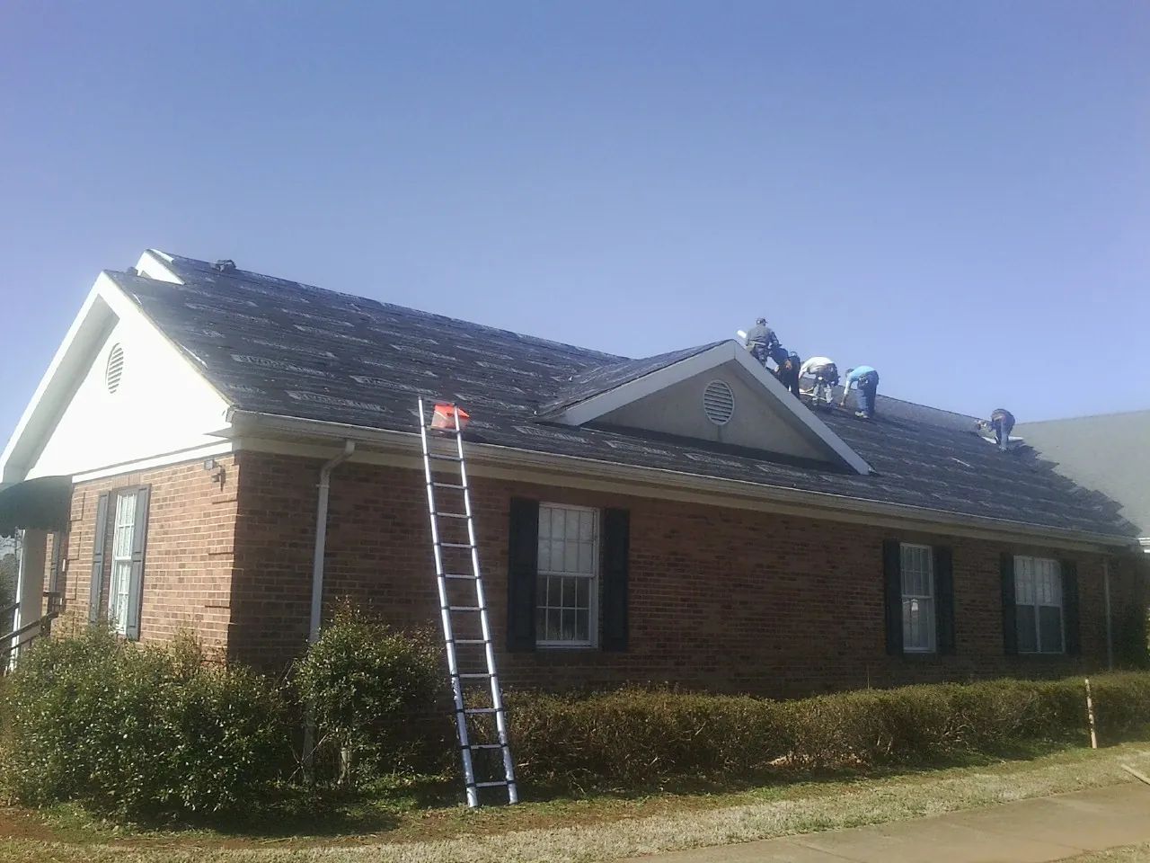 Crew tearing shingles off a brick ranch roof with a ladder set — Metal Roof Repair work by our crew in Bent Mountain