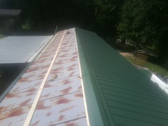 Old rusted panels beside newly installed green metal roofing — Wind Damage Roof Repair by Roofing Brothers in Bent Mountain