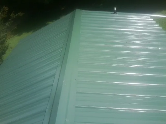New green metal panels meeting at the ridge of a roof — Flat Roof Repair work by our crew in Bent Mountain