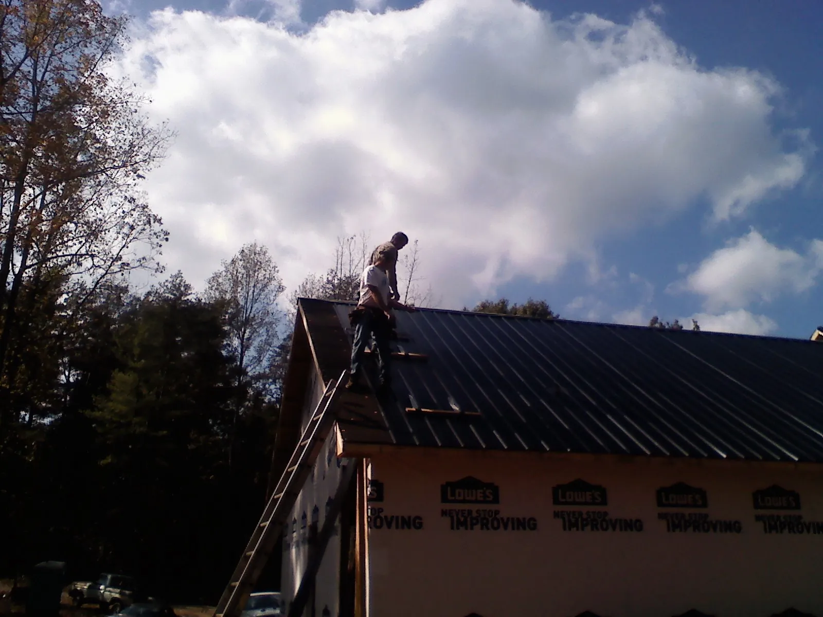 Roofer fastening dark metal panels high against a cloudy sky, from a Roof Inspection job in Bent Mountain
