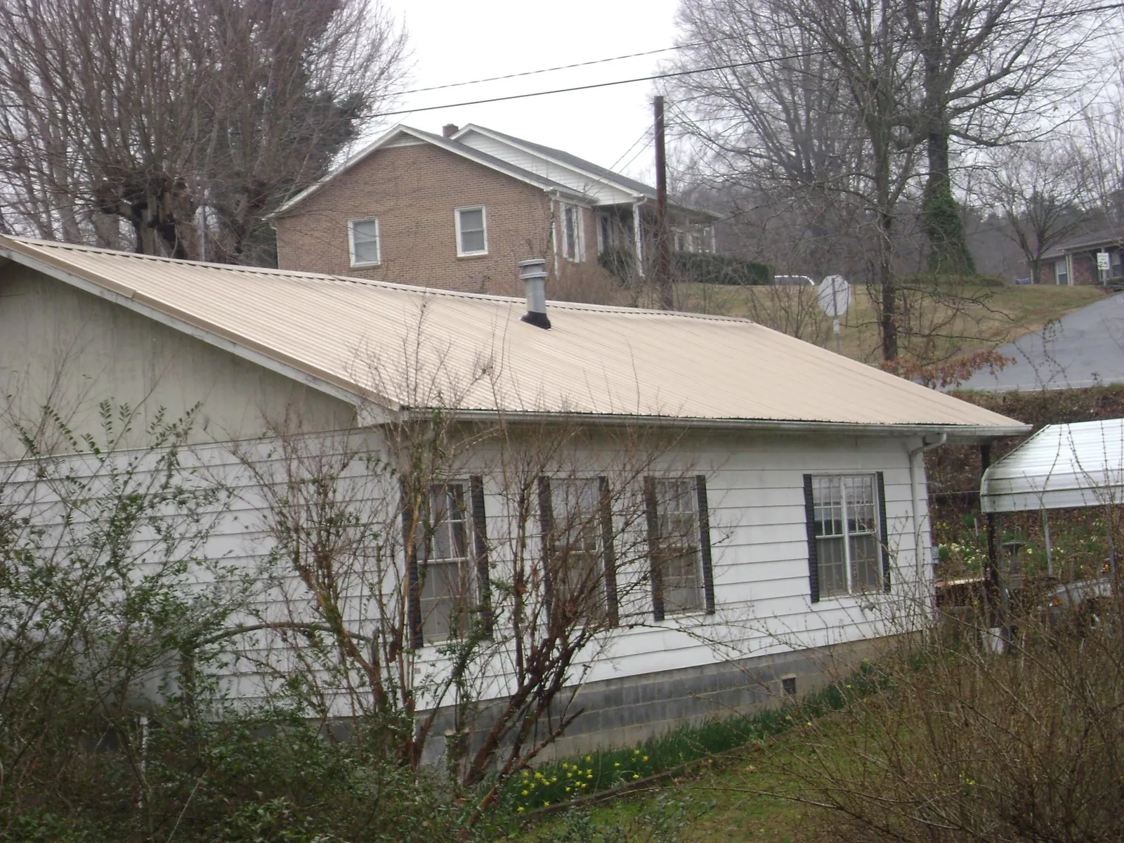 Tan metal roof on a white sided house set into a hillside — Commercial Roofing by Roofing Brothers in Bent Mountain