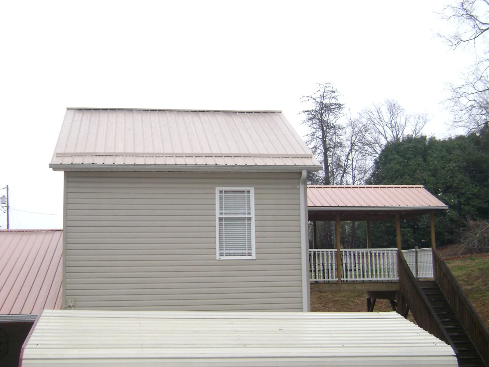 Tan metal roofs on a two story addition and attached porch, from a Roof Replacement job in Bent Mountain